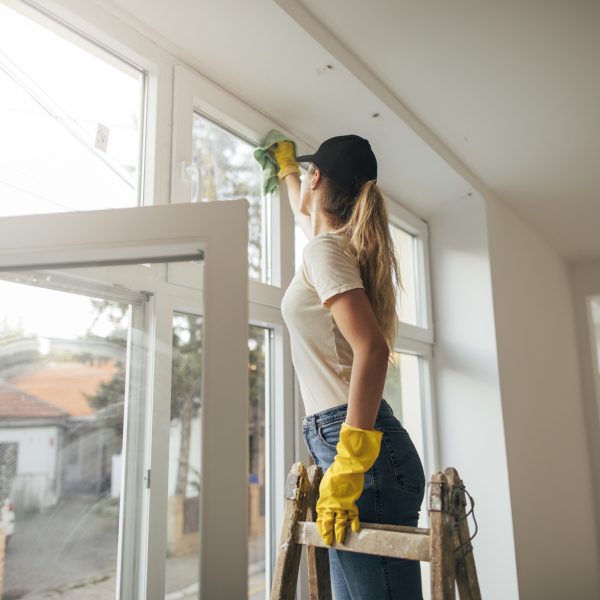 Woman in yellow gloves cleaning window with rag.